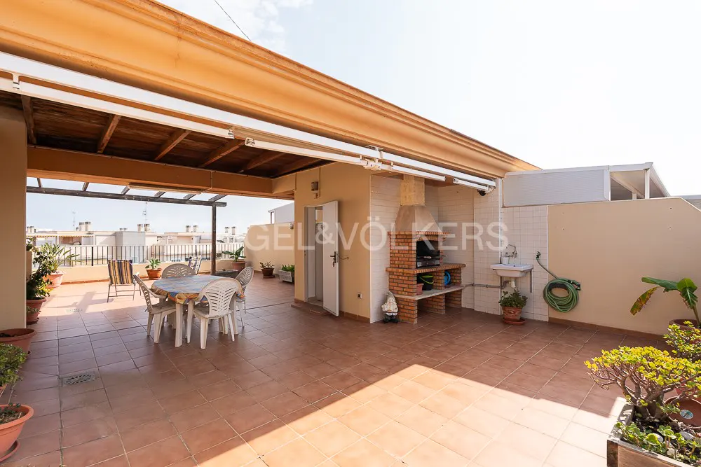 A rooftop patio with a table, chairs, a brick barbecue, and potted plants.
