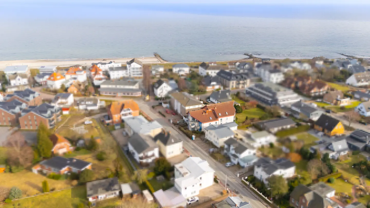 Aerial view of a coastal town with houses, trees, and the ocean in the background.