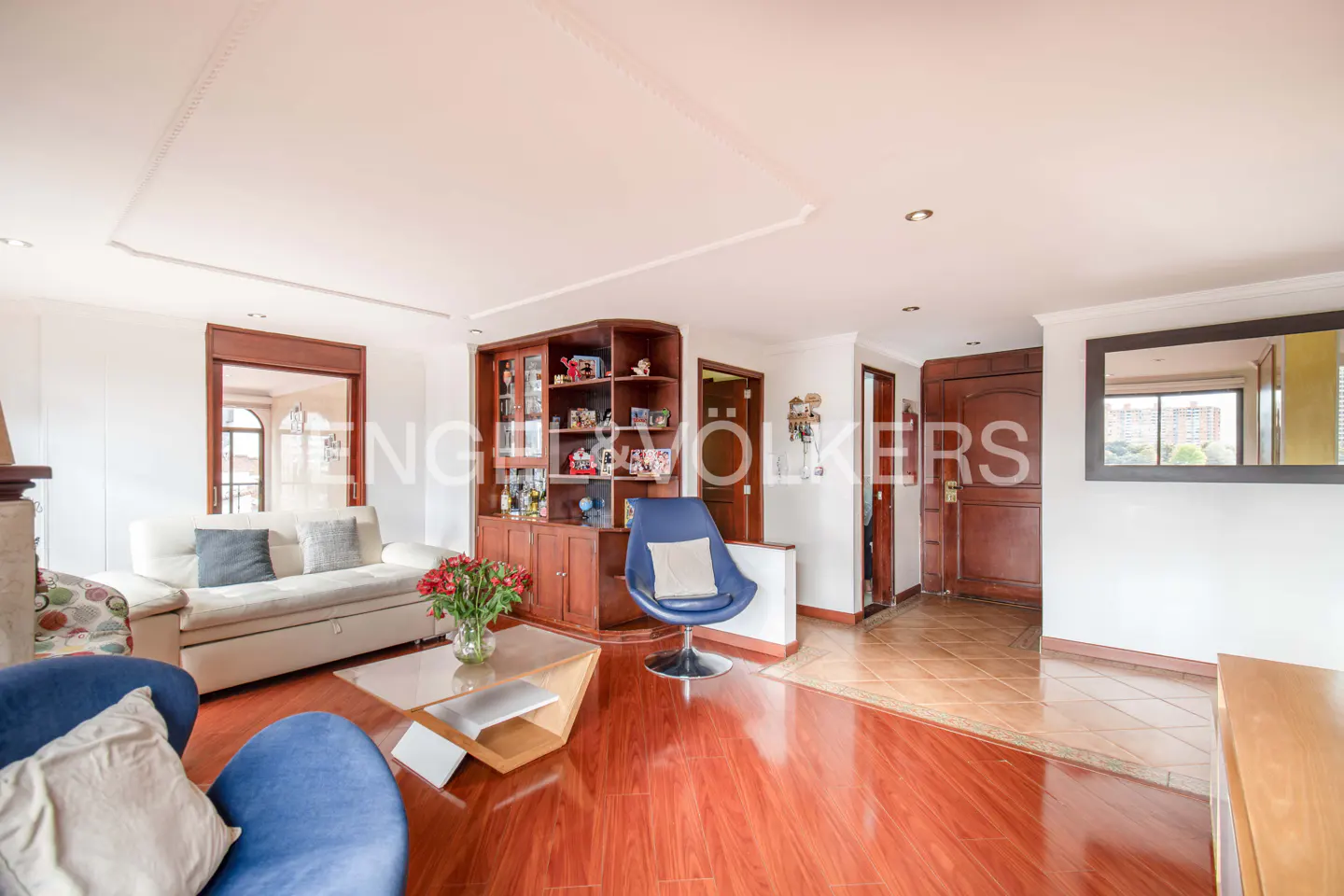 A living room with hardwood floors, a white sofa, a blue chair, and a wooden cabinet.