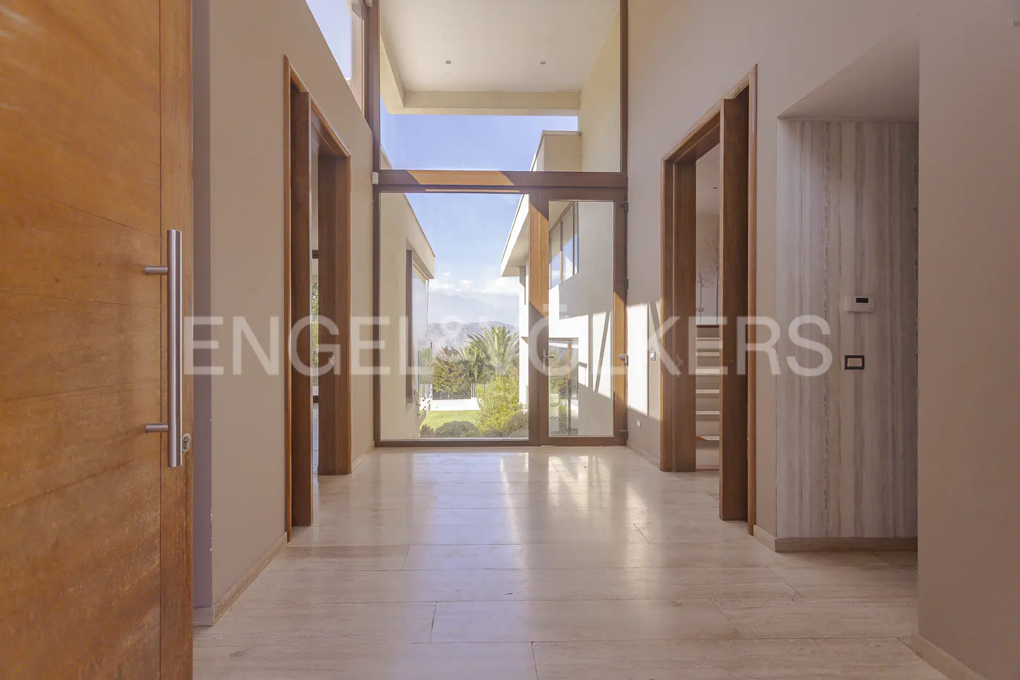 Modern home foyer with marble floors, wooden doors, and a large glass window showcasing the exterior landscape.
