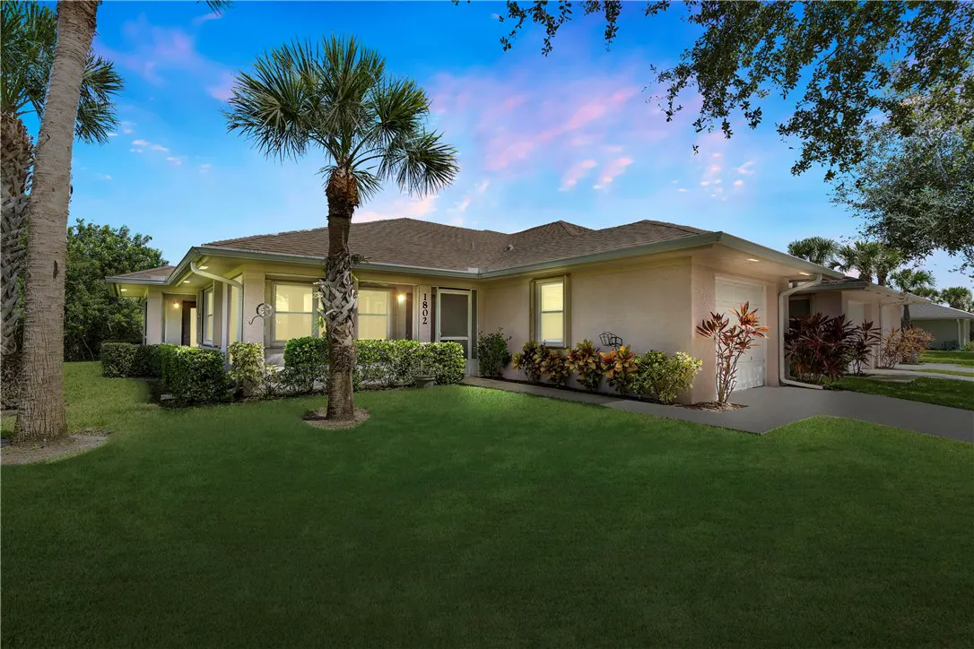 Single-story beige house with a palm tree in the front yard under a sunset sky.