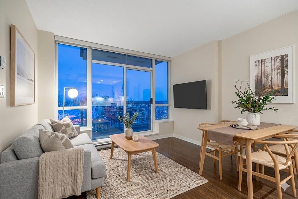 Living room with a gray sofa, wood table, dining set, and a large window with a city view at night.