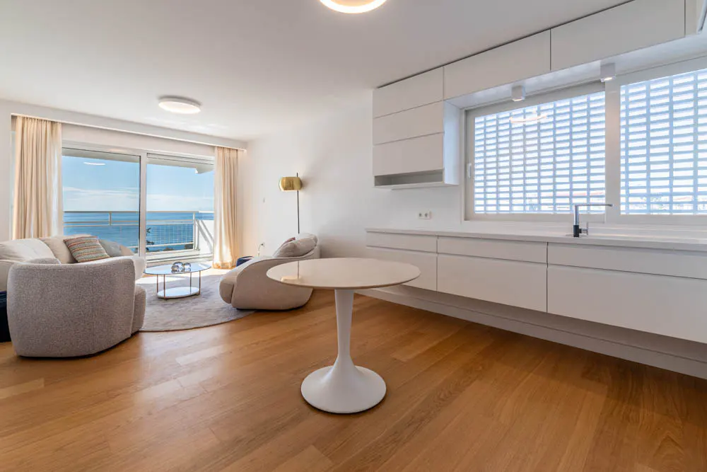 Bright, modern apartment interior with wood floors, white kitchen cabinets, and a living area with ocean views.