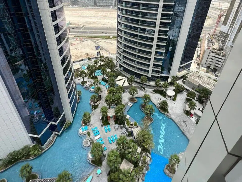 Aerial view of a blue pool area with lounge chairs and palm trees between two modern high-rise buildings.
