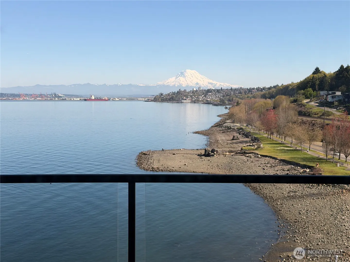 Water view from a balcony. Distant snow-capped mountain, city, and shoreline visible. Blue sky.