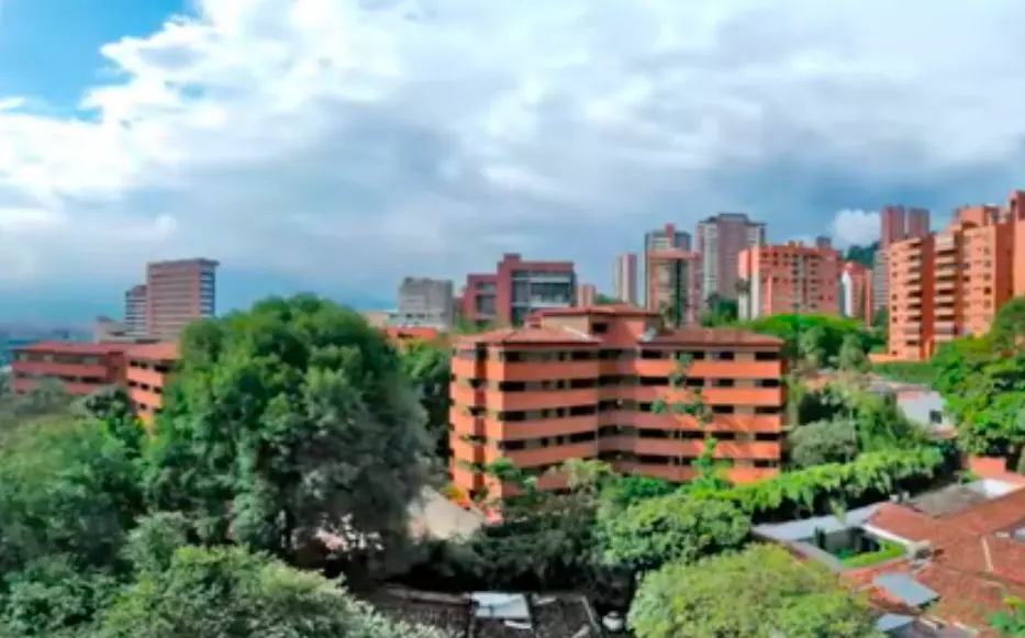 Cityscape view with red brick buildings and lush green trees under a cloudy sky.