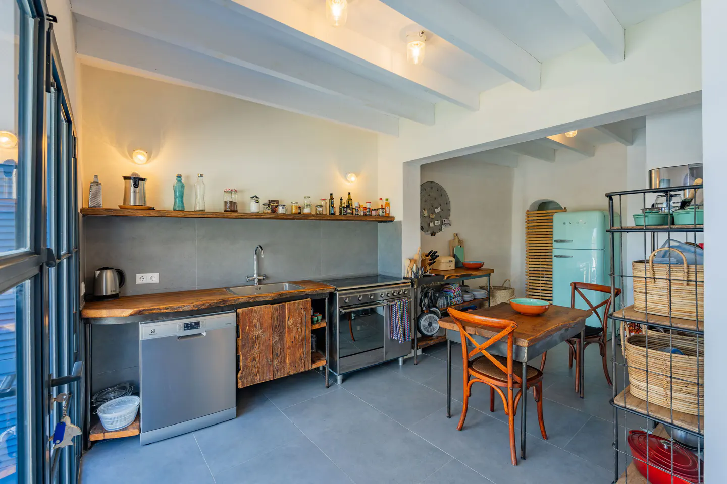 A modern kitchen with a wood countertop, stainless steel appliances, and a vintage turquoise refrigerator. A wooden table and chairs are in the center.