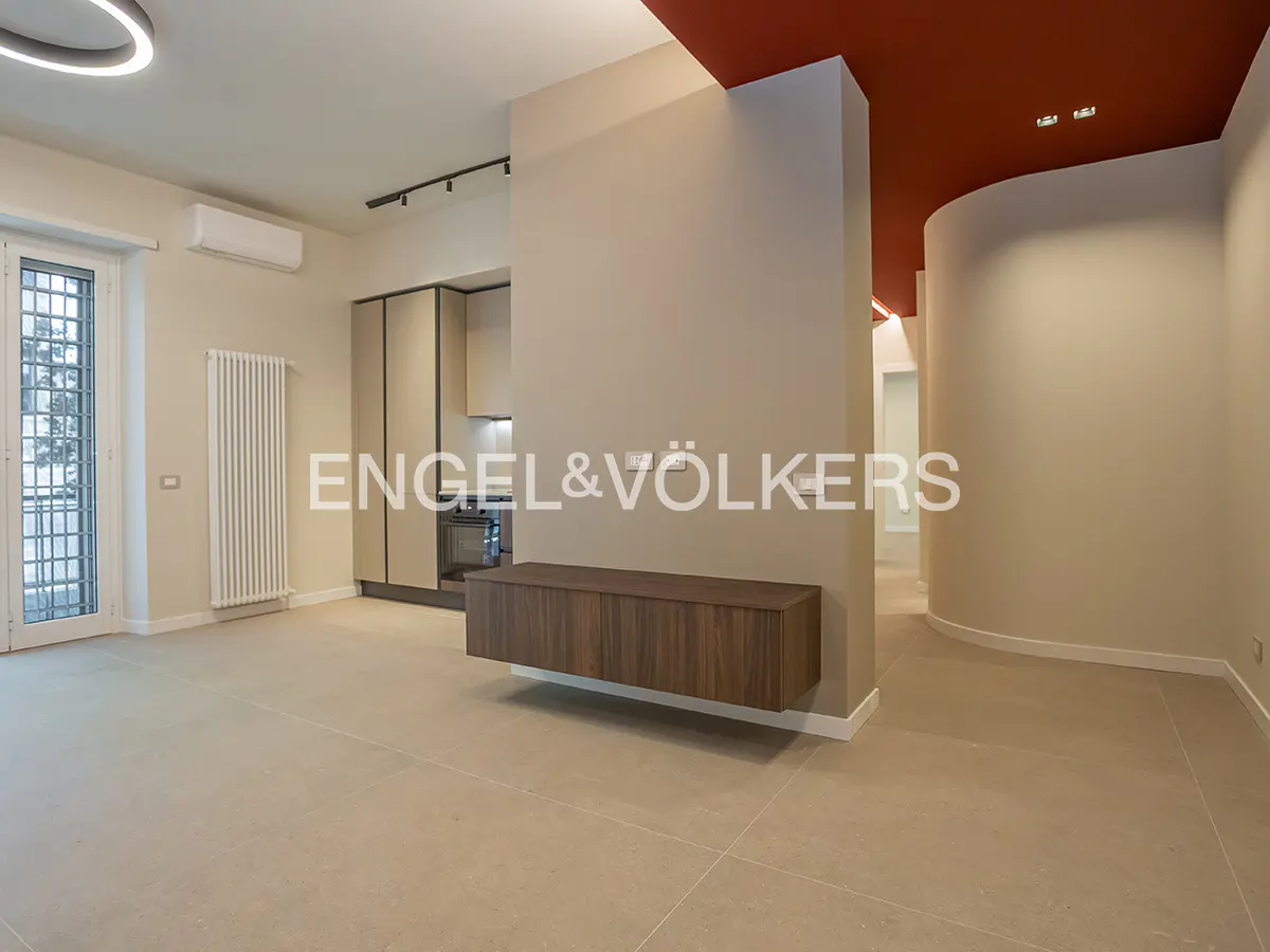 A modern apartment interior with beige walls, a red ceiling accent, and a sleek kitchen area.