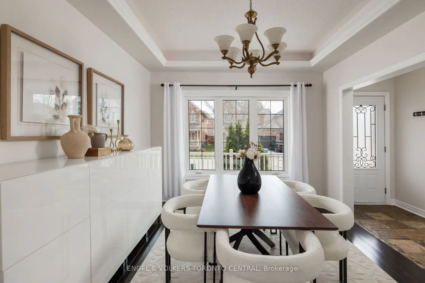 Bright dining room with white walls, a dark wood table, and white chairs. A white cabinet sits against the wall with framed art above.
