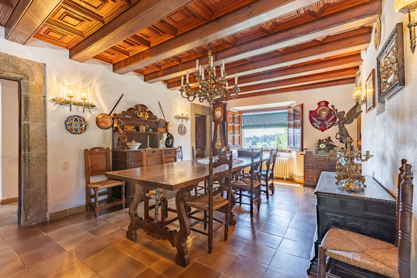 A dining room with a wooden table, chairs, and a chandelier. The room has a wooden ceiling and tile floors.