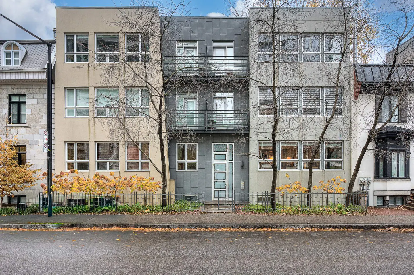 Three-story townhouses in beige, gray, and dark gray, with balconies, windows, and bare trees in front.