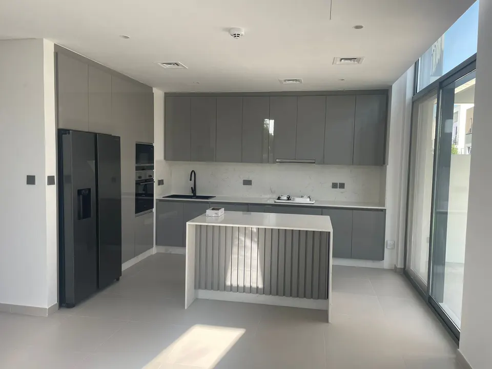 Modern kitchen with grey cabinets, white marble countertops, a central island, and a black refrigerator.