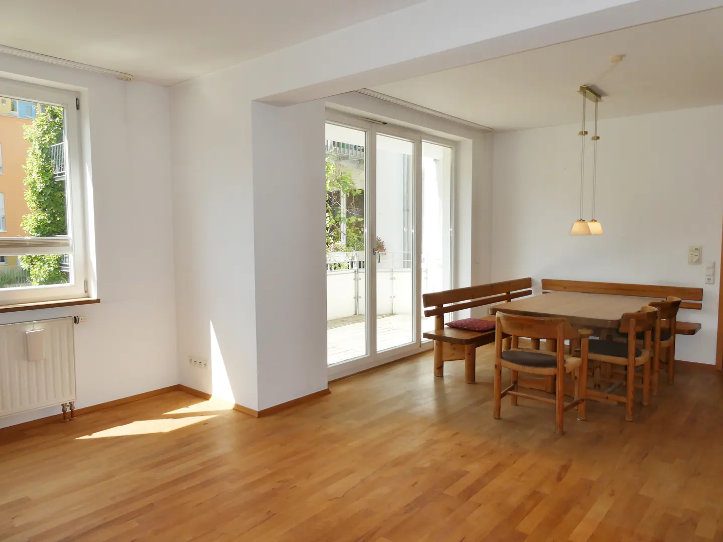 Bright dining area with wooden floors, a wooden table, chairs, and bench, plus glass doors leading to a balcony.