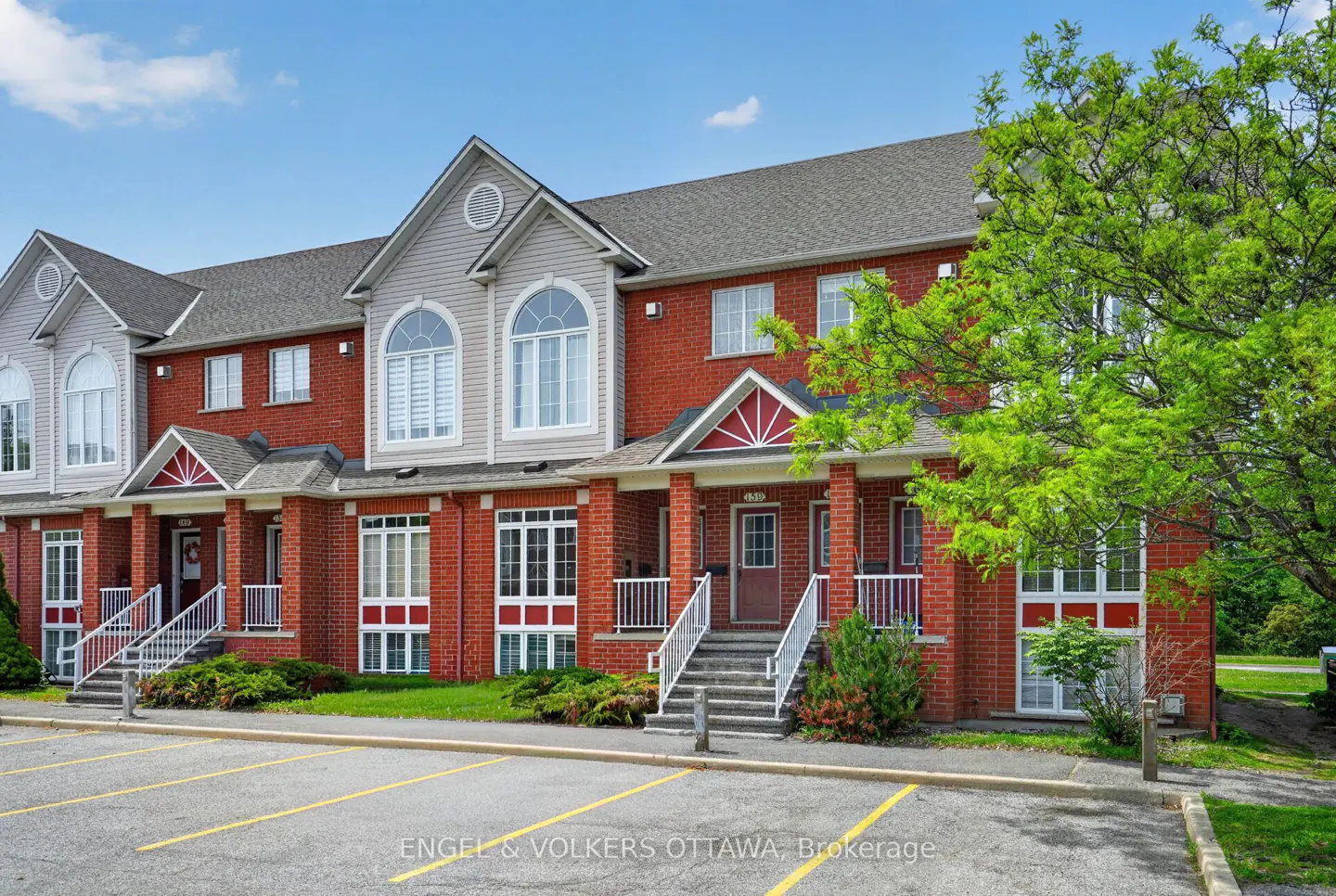 Exterior view of a red brick townhouse complex with grey siding, white trim, and a parking lot in the foreground.