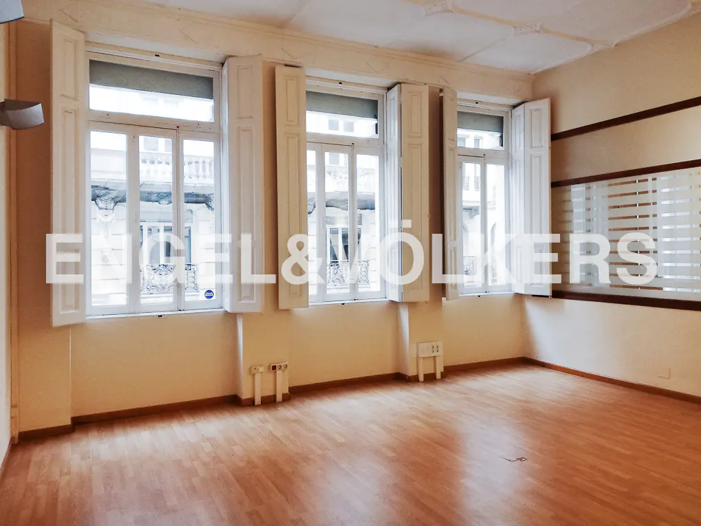 Empty room with wood floors, cream walls, and three large windows with white shutters. The Engel & Volkers logo is superimposed.
