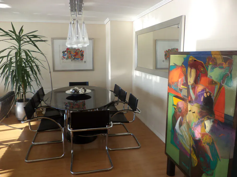 Dining room with black table, chrome chairs, and colorful art. A large plant sits in the corner.