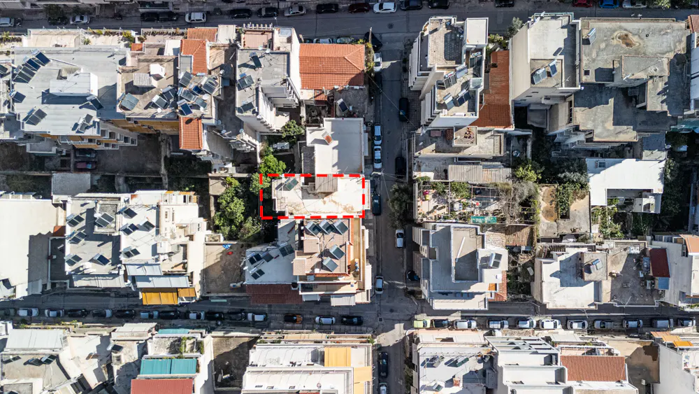Aerial view of a building with solar panels, surrounded by other buildings and a red dashed line.