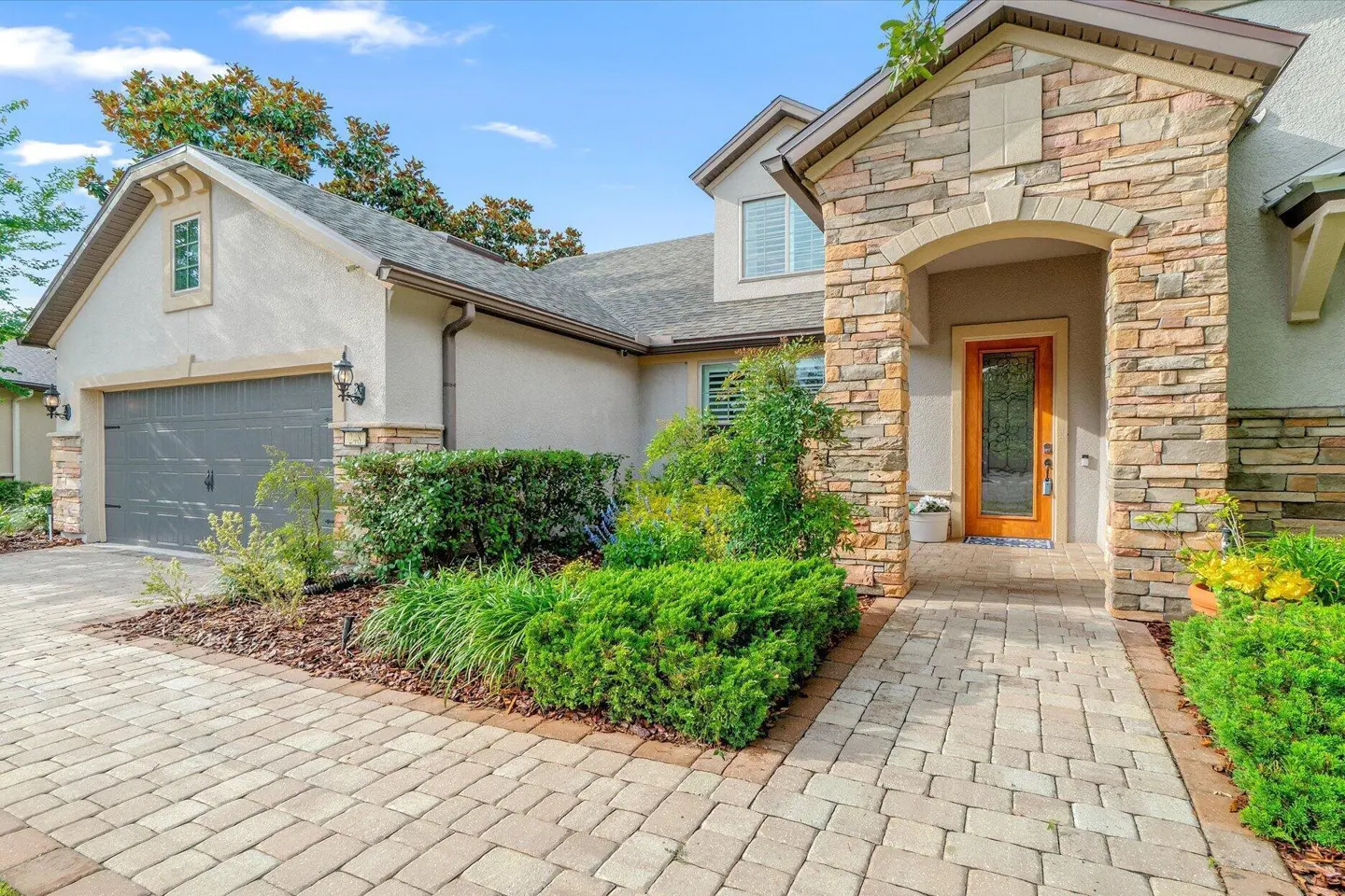 Exterior of a suburban home with a stone-accented entryway, a gray garage, and a paved walkway surrounded by greenery.