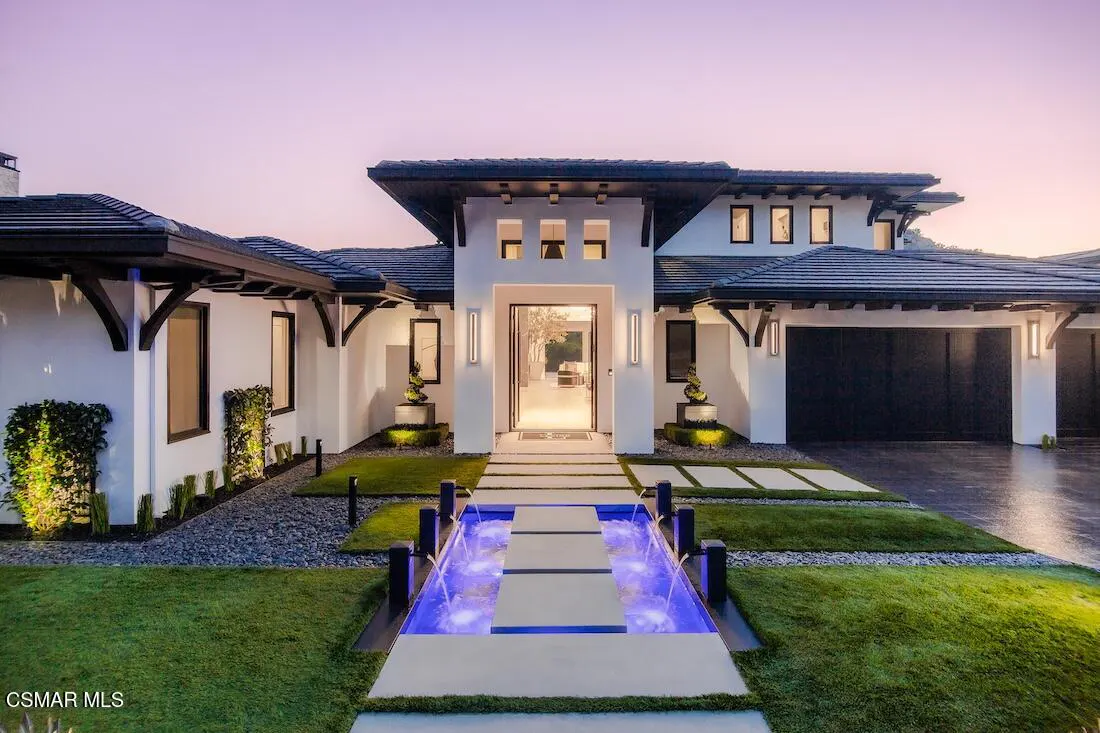 Exterior of a modern white house with black trim, a water feature, and a purple sky.