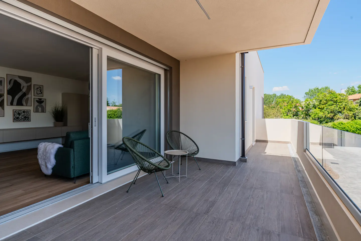 Balcony with two green chairs and a small table, sliding glass doors to the interior, and a view of trees in the background.
