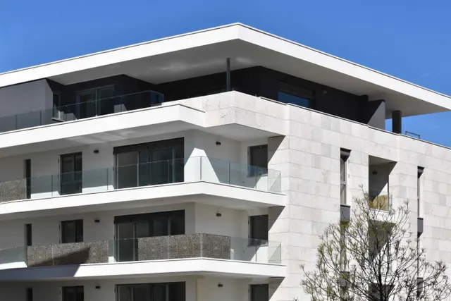 Modern white apartment building with glass balconies under a clear blue sky.