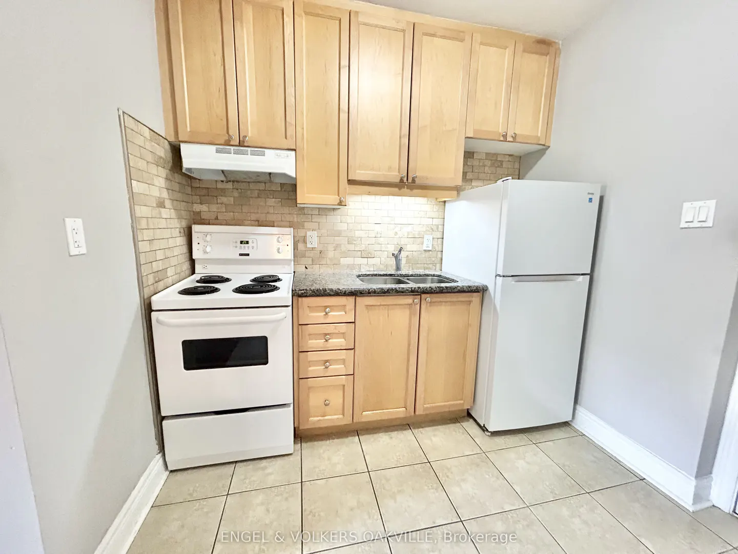 A kitchen with light wood cabinets, a white stove and refrigerator, and a tiled backsplash.
