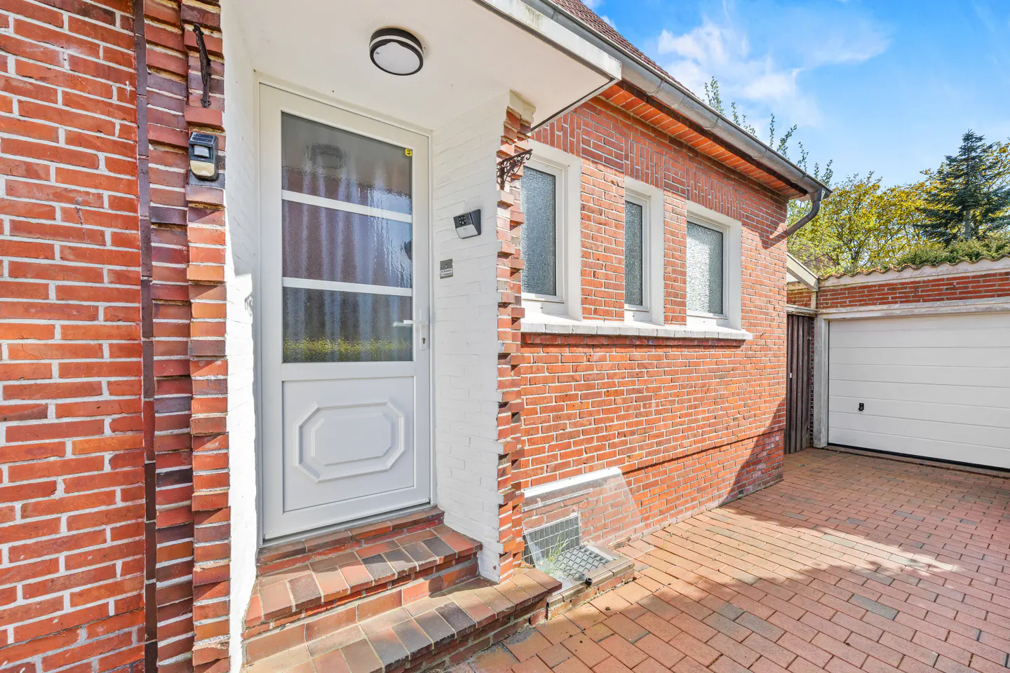 Red brick house exterior with a white front door, steps, and a white garage door on a brick driveway.