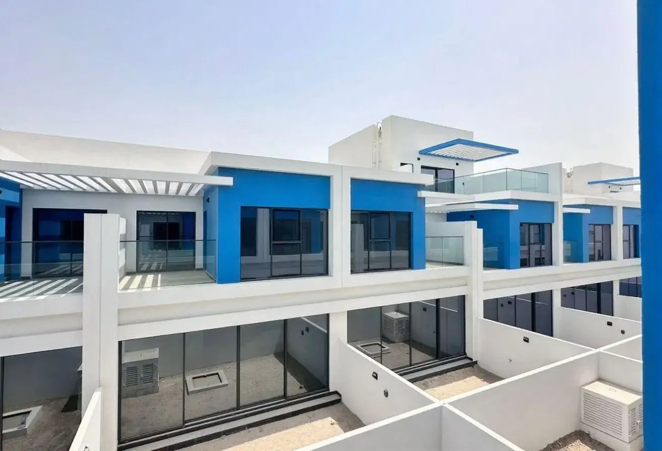 Exterior view of modern townhouses with blue accents and white walls, featuring balconies and large windows.