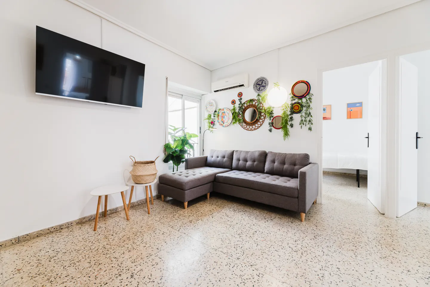 Bright living room with a gray sectional sofa, TV, and decorative wall art. Open doorway leads to another room.