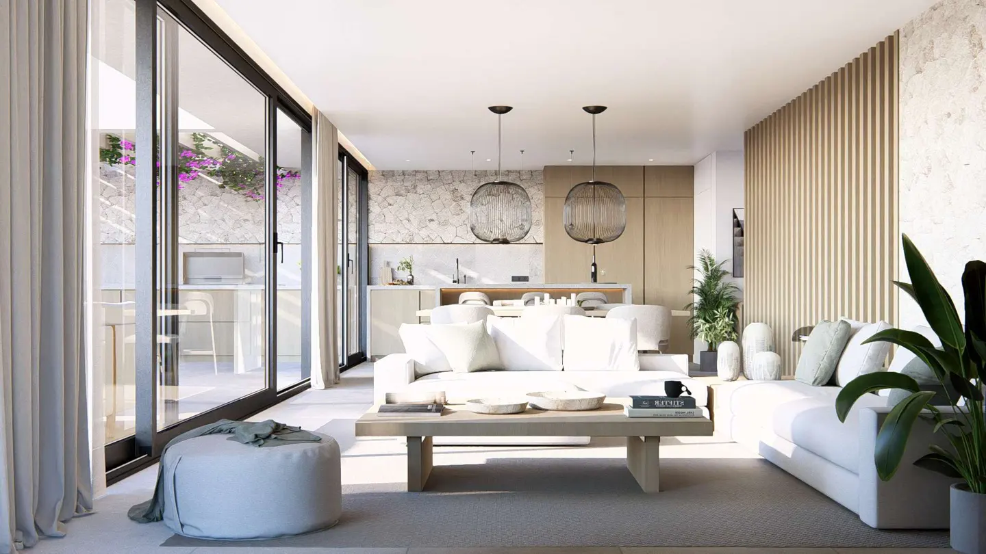 Bright, open-concept living space with white sofas, wood table, and pendant lights. Sliding glass doors lead to a patio with purple flowers.