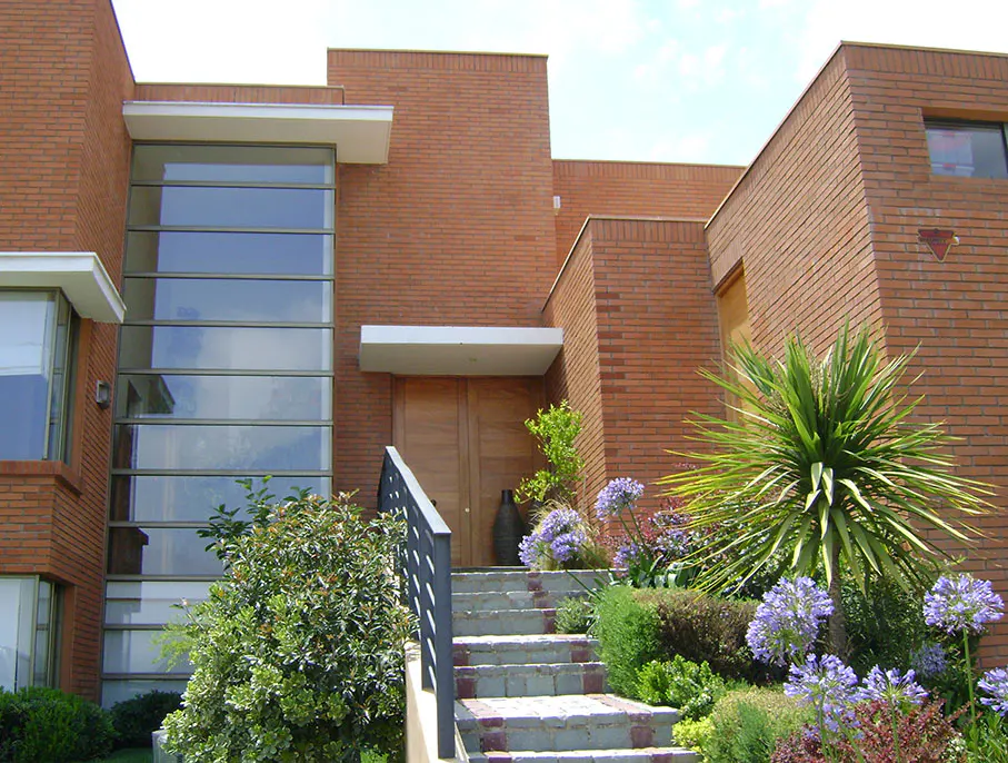 Brick house with a modern design, featuring a large window, wooden door, and landscaped front yard with stairs.