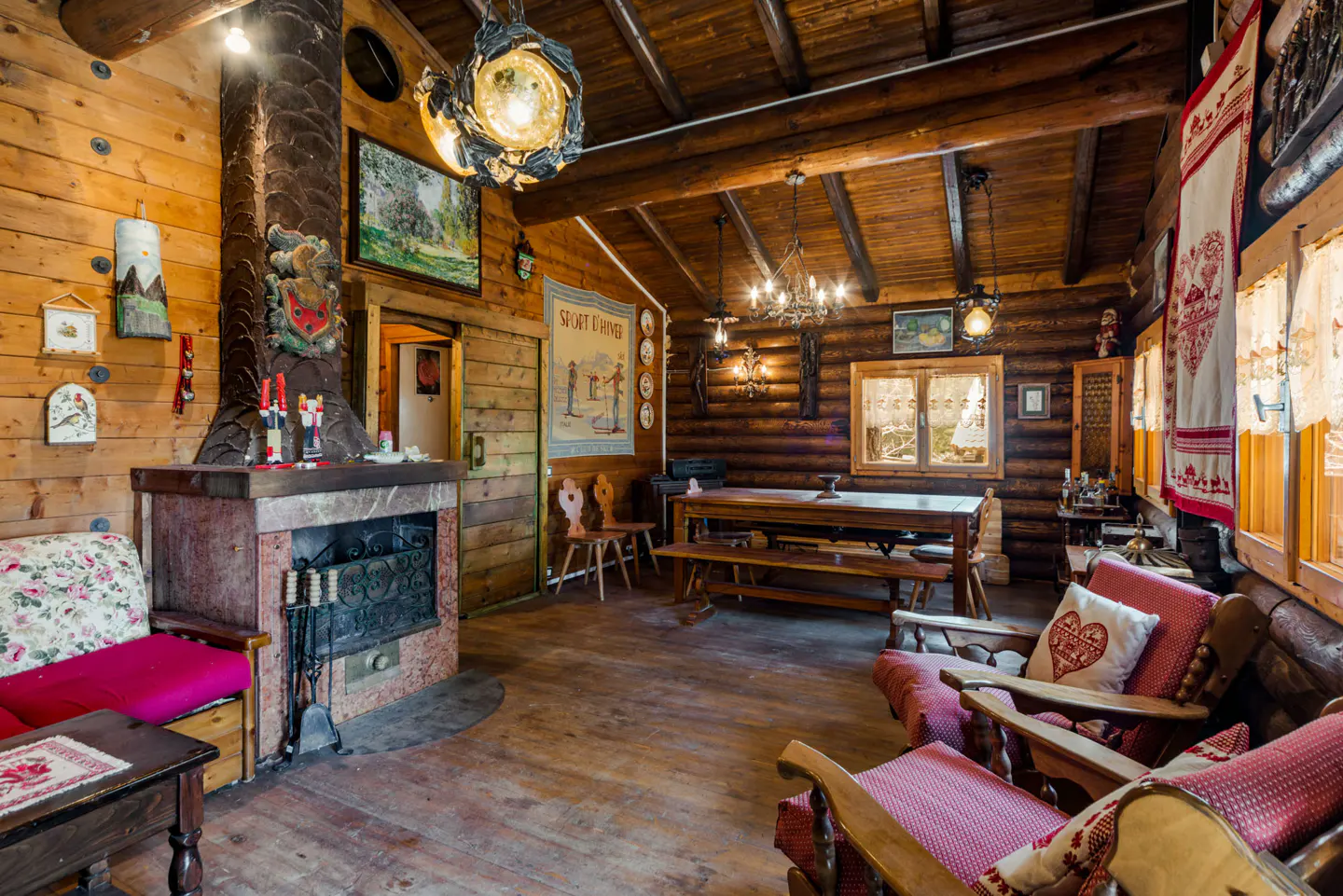 Rustic log cabin interior with a stone fireplace, wooden furniture, and decorative folk art accents. Warm lighting enhances the cozy atmosphere.