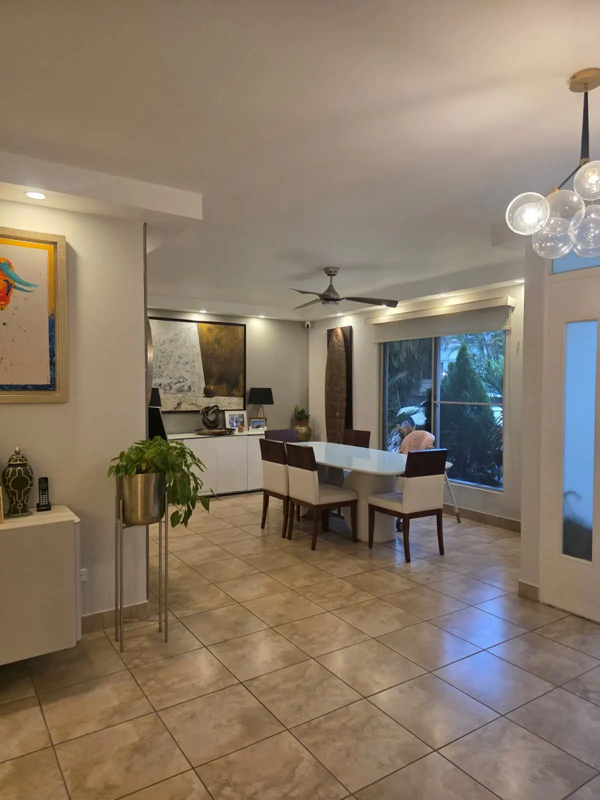 Open-concept living and dining area with tile floors, white walls, and modern art. A white dining table with six chairs is visible.