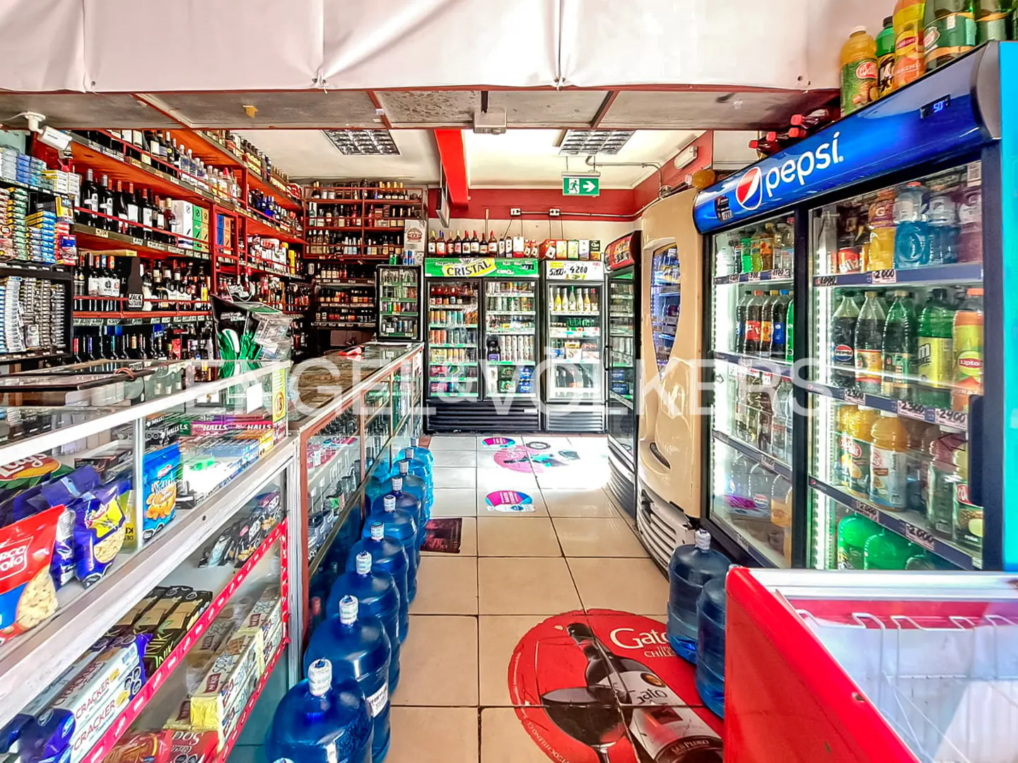 Inside a small grocery store with shelves stocked with liquor, snacks, and drinks in coolers.