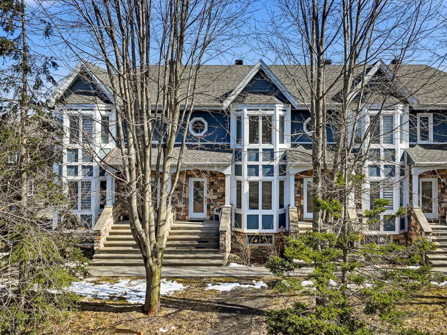 Exterior view of blue townhouses with stone accents, white trim, and multiple windows. Trees frame the building.