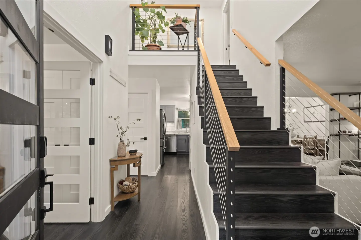 Modern entryway with dark wood stairs, cable railings, light wood handrails, and a console table leading to the kitchen.