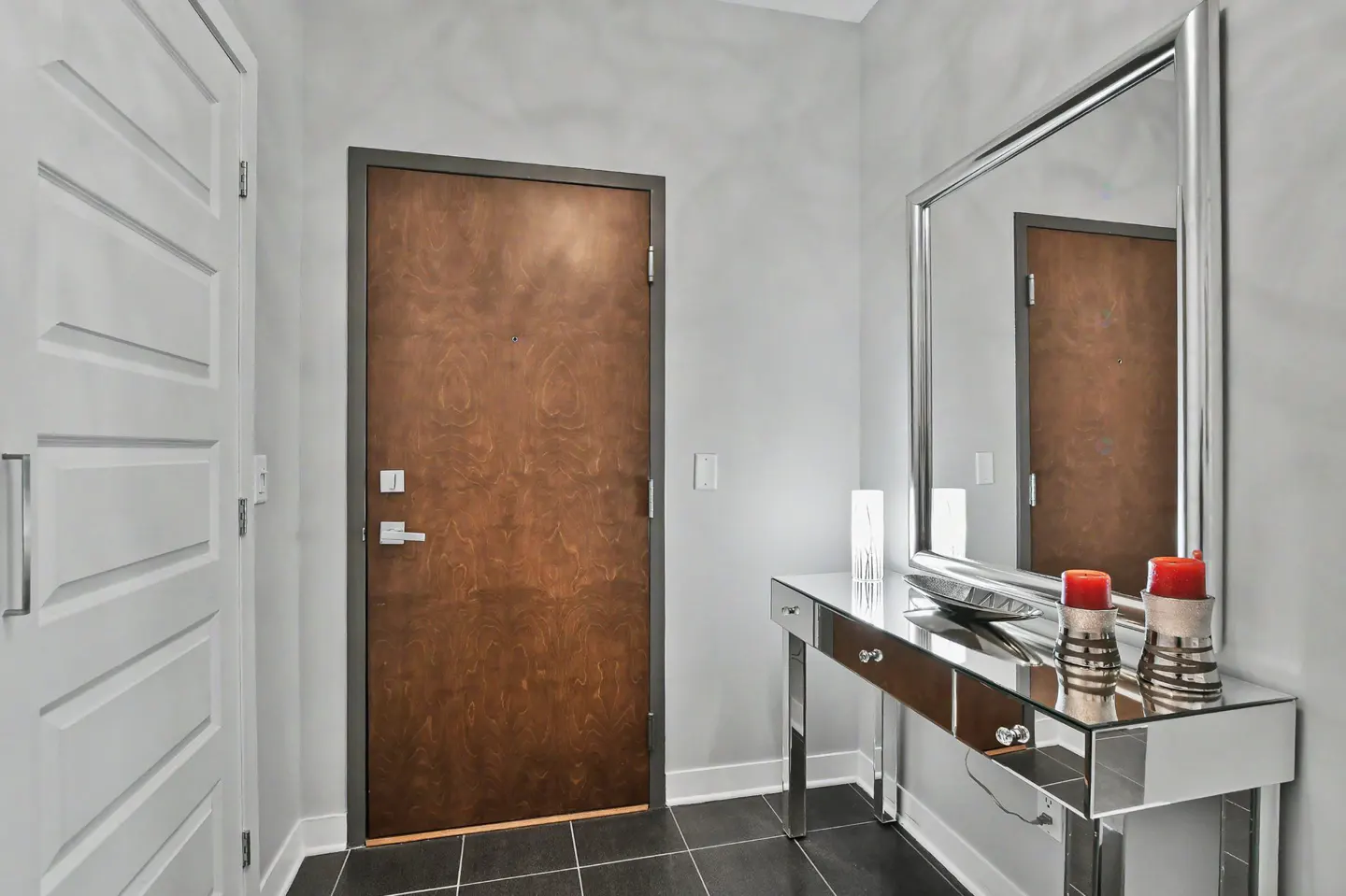 Entryway with a brown door, white door, and mirrored console table with red candles.