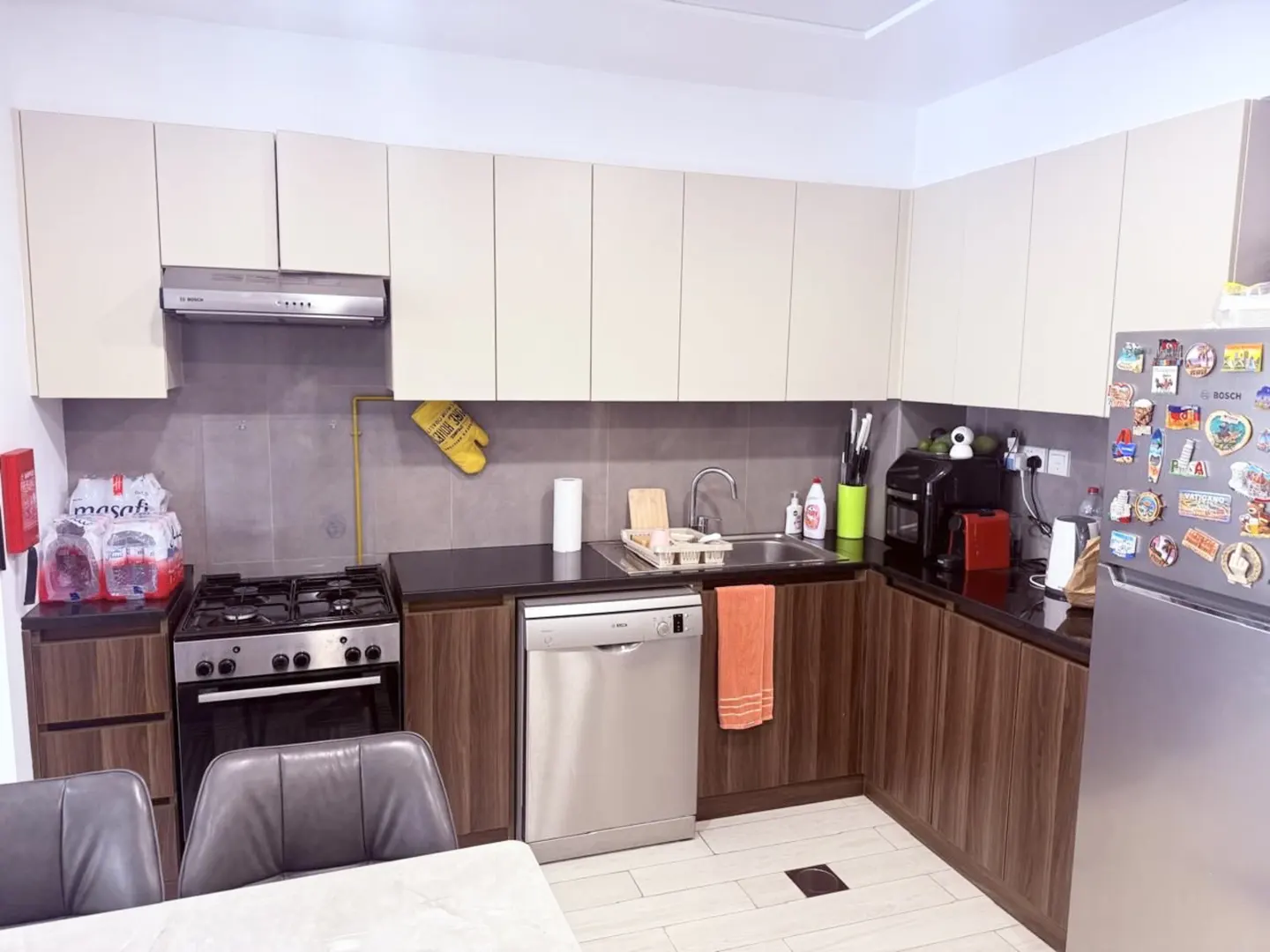 A well-lit kitchen with beige cabinets, dark countertops, and stainless steel appliances. A gas stove, dishwasher, and refrigerator are visible.