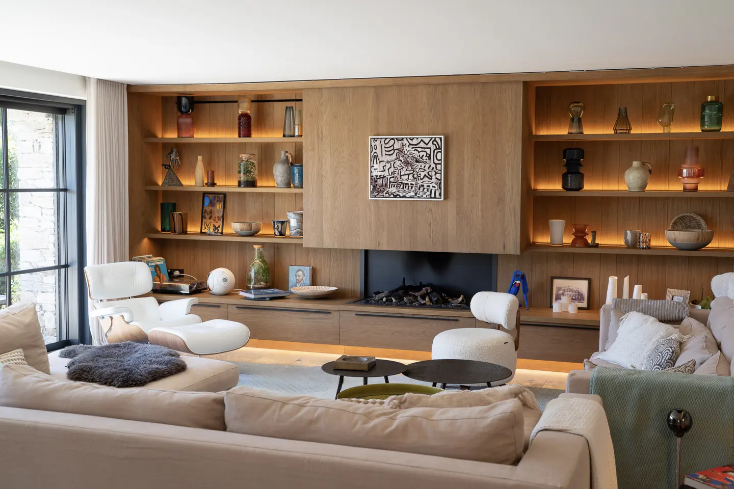 Living room with a light beige sofa, a fireplace, and built-in wooden shelves with decorative items and warm lighting.