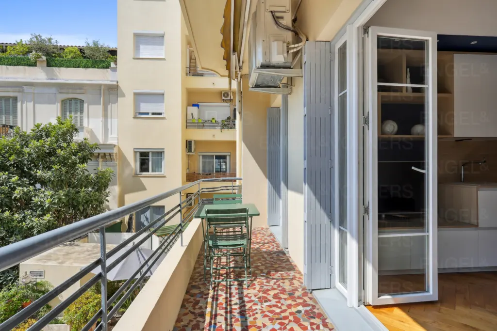 Balcony view with green table and chairs, colorful tiled floor, and open doors to a kitchen.