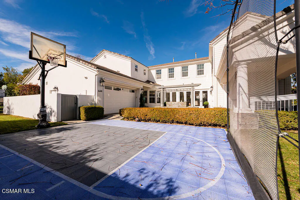 Backyard view of a two-story white house with a blue and gray basketball court and a basketball hoop.