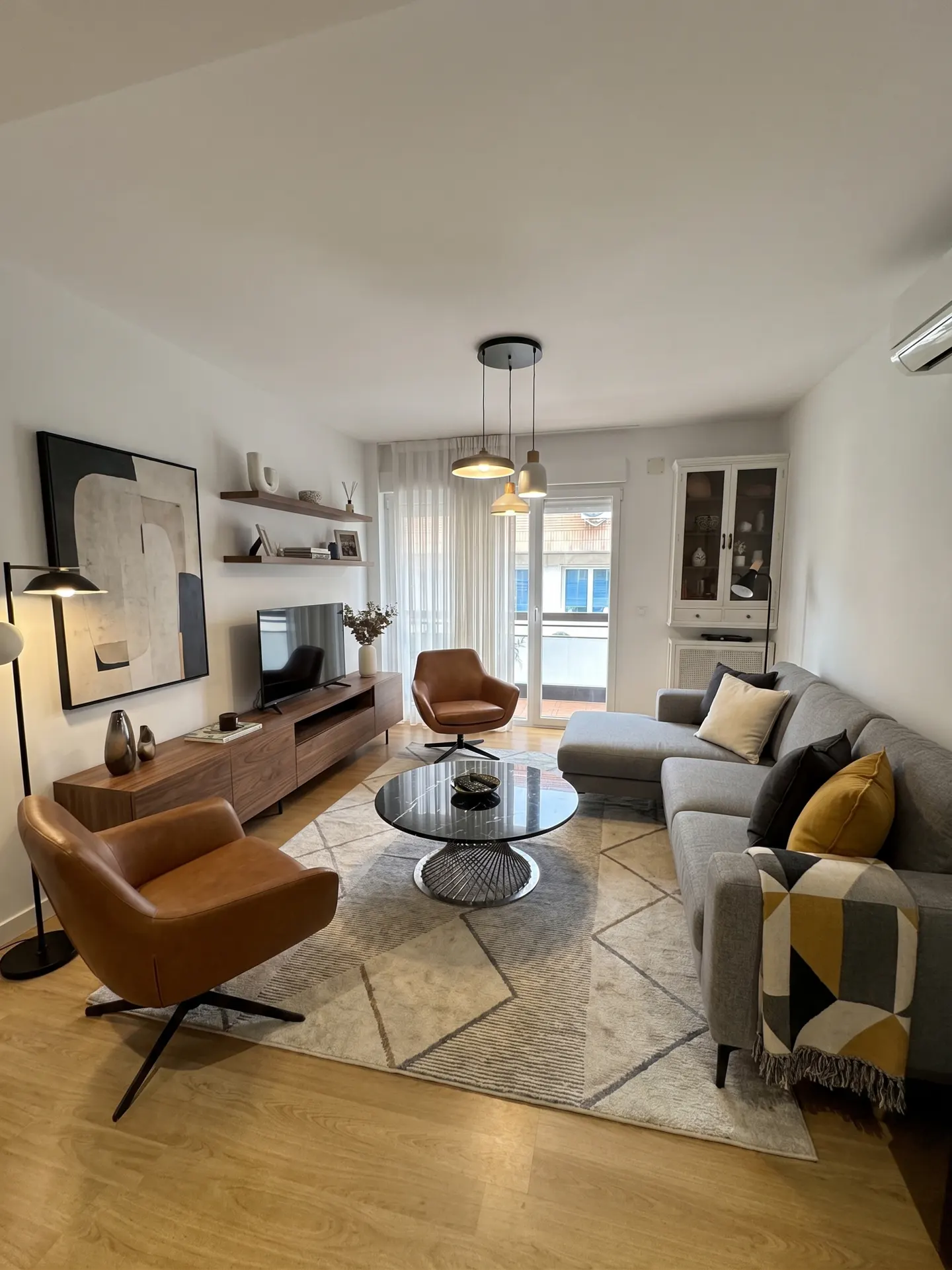 Modern living room with a grey sectional sofa, two tan leather armchairs, a round coffee table, and a wooden media console.