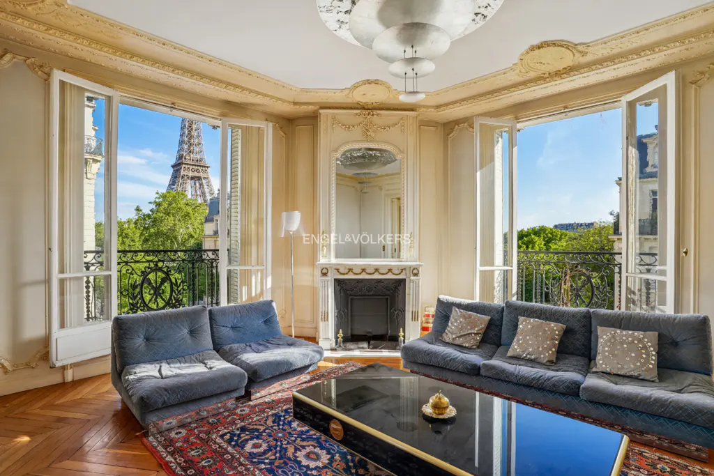Living room with Eiffel Tower view. Two blue sofas face each other over a black coffee table on a patterned rug. Fireplace and mirror on wall.