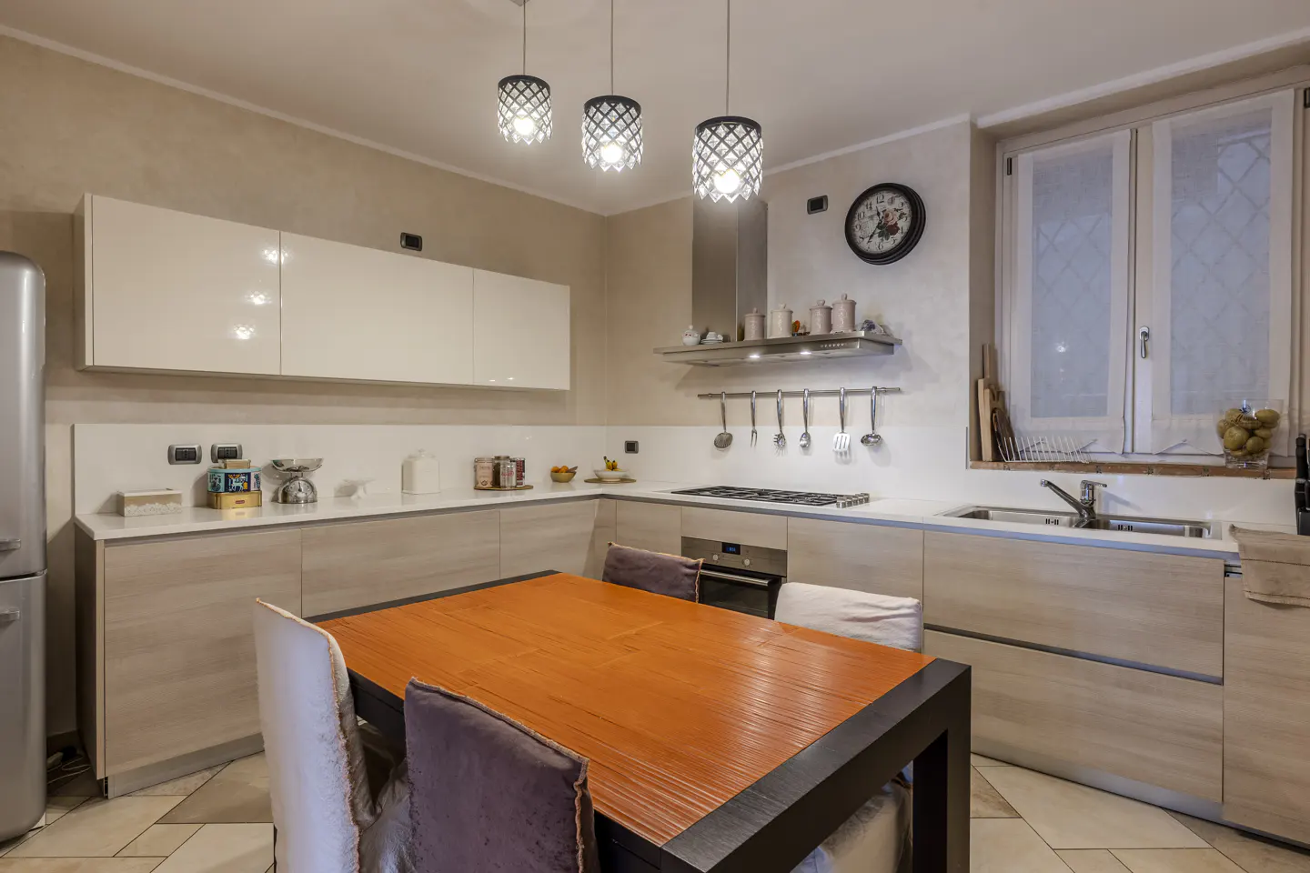 Modern kitchen with light wood cabinets, white countertops, a dining table with orange top, and three pendant lights.