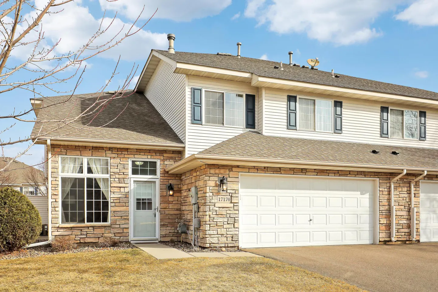 Exterior view of a two-story townhouse with stone and white siding, a two-car garage, and a well-maintained lawn.