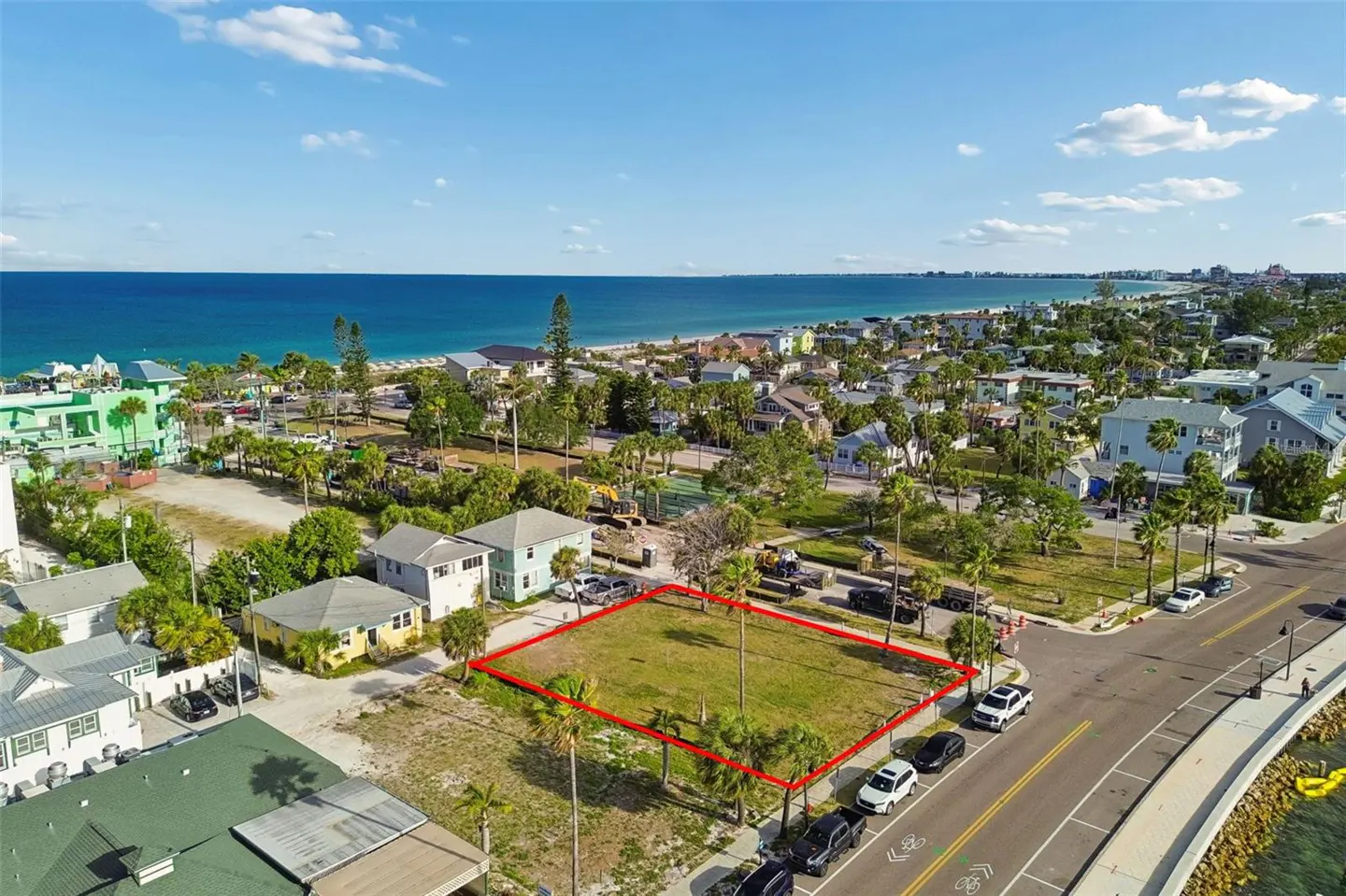 Aerial view of a vacant lot outlined in red, near a beach, houses, and a road with parked cars.
