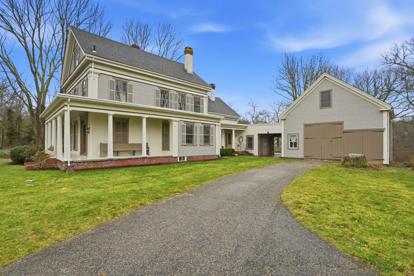 Exterior view of a two-story house with a gray roof, white pillars, and a long driveway leading to a detached garage.