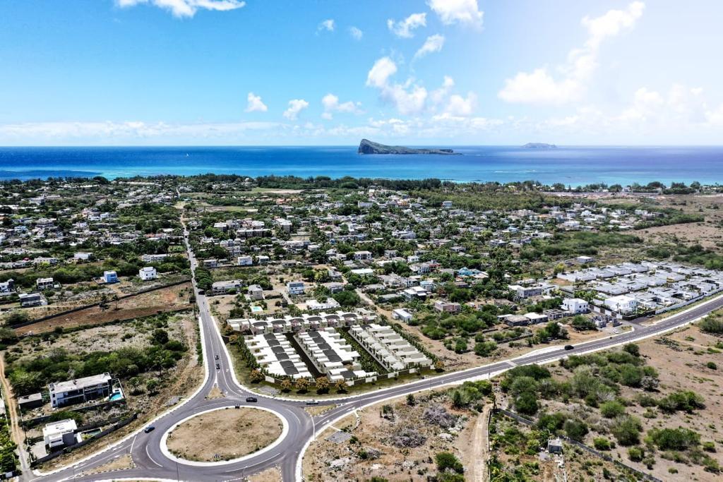 Aerial view of a coastal town with houses, trees, and a roundabout. The blue ocean and sky are visible in the background.