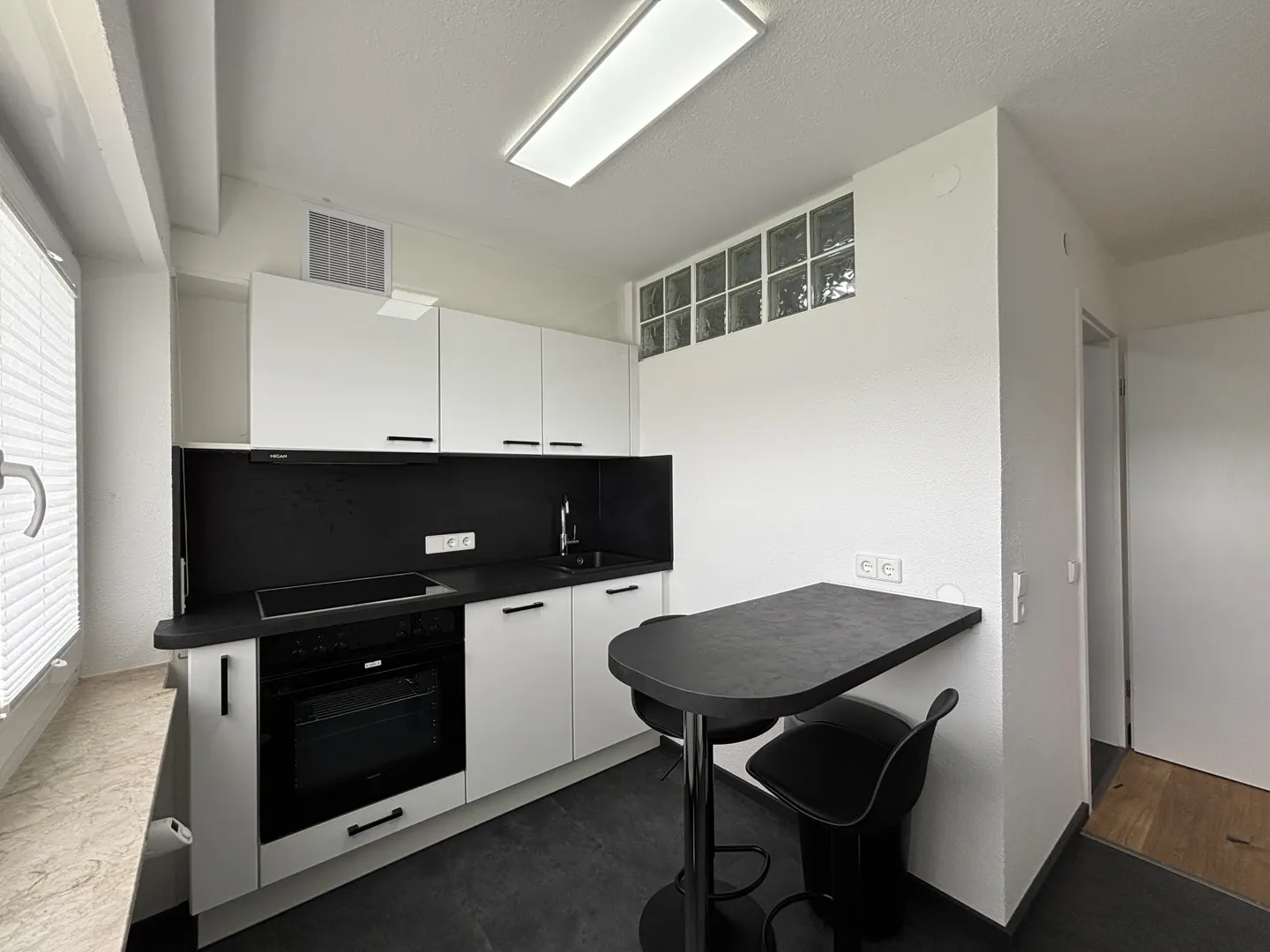 A modern kitchen with white cabinets, black countertops, and a black breakfast bar with two stools.
