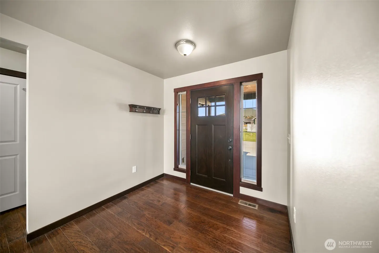 Entryway with dark wood door, sidelights, and trim. Hardwood floors and light gray walls. Coat rack on the wall.